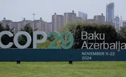 A large sign on a green lawn says COP20 Baku Azerbaijan with tall buildings in the background